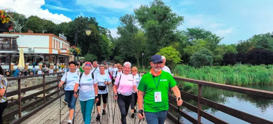 Grupa uczestników maszeruje z kijkami Nordic Walking po drewnianym pomoście